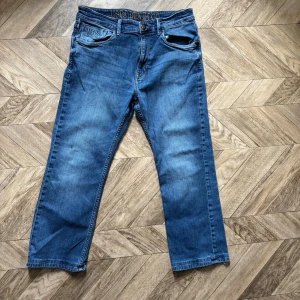 Blå jeans från USPA Denim Co - Snygga blå jeans från USPA Denim Co med klassisk femficksdesign och broderad logga på fickan. Jeansen har raka ben och normal midja. Perfekta för en avslappnad och trendig look.