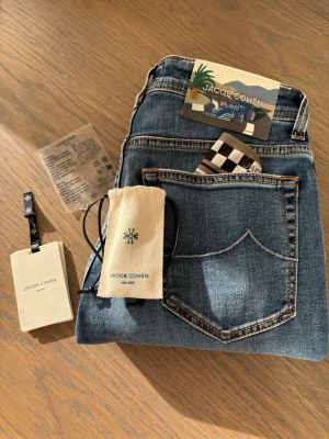 Blå jeans från Jacob Cohen - Helt ubrukte og fast pris heller ingen trades Nypris 6-7 tusen og eneste paret på hele plick brukt en håndfull ganger  Snygga blå jeans från Jacob Cohen med klassisk femficksmodell och kontrastsömmar. Jeansen har en patch med motiv bak i midjan och detaljer som ger en exklusiv känsla. Tillverkade i mjukt denimtyg, perfekta för en trendig och avslappnad stil.