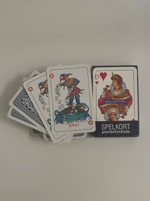 Kortlek plastbehandlade spelkort - En klassisk kortlek med plastbehandlade spelkort. Korten har traditionella motiv i färgerna röd, blå, vit och svart. Lådan visar hjärter dam och en joker. Perfekt för pokerkvällar eller kortspel med vänner.