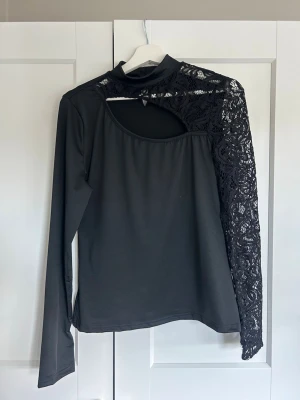 Svart topp med spets och cut out-detalj - Långärmad med cut out detalj och spetsärm. Knäpps i nacken