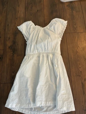 Vit kortärmad klänning med volang från H&M - Söt vit klänning med korta volangärmar och rund halsringning. Klänningen har resår i midjan och är tillverkad i ett lätt bomullstyg, perfekt för varma dagar. Enkel och stilren design som passar till många tillfällen.