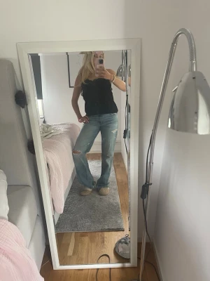 Ljusblå slitna raka jeans - Säljer ett par ljusblå jeans med raka ben och slitningar vid knäna. Jeansen har en avslappnad passform och klassisk femficksdesign. Perfekta för en trendig och avslappnad look.