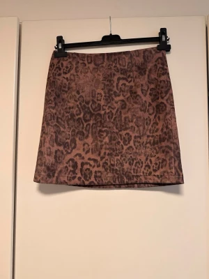 Brun leopardmönstrad kortkjol - Säljer en snygg kortkjol i brun ton med leopardmönster. Kjolen har en rak passform och dragkedja bak som detalj. Perfekt för dig som vill sticka ut lite extra med ett djurmönster.