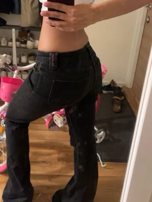 Svarta bootcut jeans med låg midja - Säljer ett par svarta bootcut jeans med låg midja och klassiska fickor både fram och bak. Jeansen har en snygg passform som framhäver figuren och är perfekta för dig som gillar en trendig och avslappnad stil. Materialet är stretchigt denim för extra komfort. Lite söndriga vid benen.