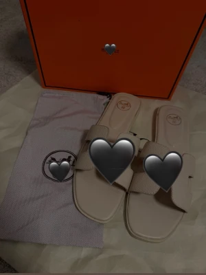 Beige slip-in sandaler med bred rem - Stilrena beige slip-in sandaler med bred, strukturerad rem och fyrkantig tå. Sandalerna har en minimalistisk design och är tillverkade i ett material som ser ut som läder. Perfekta för en trendig och avslappnad look. Funkar för 38/39 
