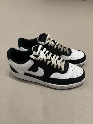 Svarta och vita sneakers med låg profil - Snygga sneakers i svart och vitt med klassisk låg siluett och perforerad tåbox. Skorna har vita snören, svart ovandel och vit sula. Materialet ser ut att vara läder eller konstläder och designen är tidlös med tydliga kontraster.