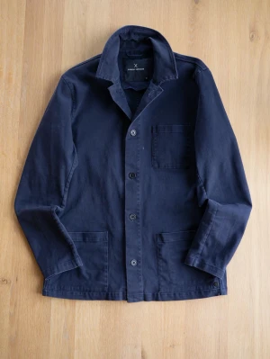 Mörkblå overshirt med knappar - Stilren mörkblå overshirt med tre fickor framtill och klassisk krage. Jackan har knäppning med fyra knappar och är tillverkad i ett mjukt bomullsmaterial. Perfekt för lager på lager och enkel att matcha.