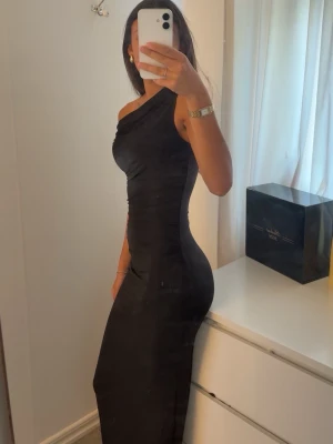 Svart oneshoulder långklänning - Snygg svart långklänning med oneshoulder-design och figurnära passform. Klänningen formar kroppen väldigt bra, aldrig kommit till användning. Pris kan diskuteras. Jag är 167 och klänningen är ungefär ner till fötterna på mig 