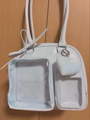 Ljusblå handväska / itabag - Söt ljusblå handväska med två genomskinliga fack framtill. Väskan har dubbla handtag och dragkedja. Perfekt för att visa upp pins eller små accessoarer. Speciellt för k-pop fäns. 
