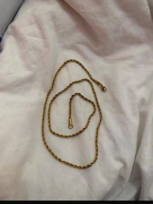 Guldigt Cordell halsband  - Säljer ett stilrent guldfärgat halsband med tvinnad kedja. Halsbandet har en enkel och klassisk design som passar till många olika stilar. Materialet ser ut som metall med guldfinish och låset är diskret och smidigt.