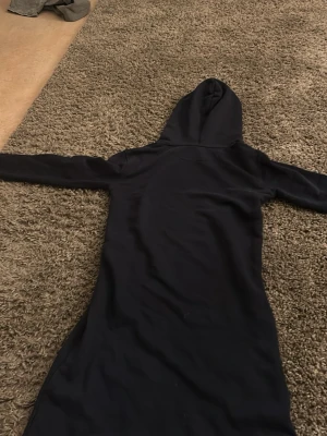 Mörkblå hoodieklänning från GANT - Snygg mörkblå hoodieklänning från GANT med vit logga på bröstet och stor magficka. Långärmad modell med huva och dragsko. Perfekt för en chill och avslappnad stil. Mjuk och skön bomullskänsla. (Made in china) 