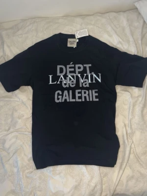 Gallery dept x lanvin - Svart t-shirt från Gallery Dept. med tryck i vitt och grått framtill där det står 'DÉPT LANVIN de la GALERIE'. Klassisk rund hals och korta ärmar. Skön och stilren modell i mjukt bomullstyg. Oversized i storlek M
