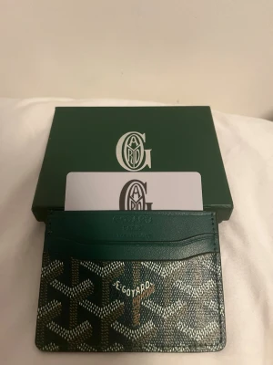grön korthållare - Snygg grön korthållare från klassiskt mönster i vitt och grått. Kommer med originalask, dammduk och kort. Perfekt för dig som vill ha en exklusiv och stilren accessoar i fickan.