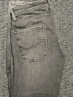 Grå jeans från Jack & Jones - Snygga grå jeans från Jack & Jones med klassisk femficksdesign och diskret broderad bakficka. Jeansen har normal midja och raka ben. Tillverkade i mjuk denim som ger en avslappnad look.
