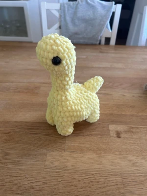 Virkad gul dinosaurie - Söt handgjord dinosaurie i mjukt, gult garn med stora svarta säkerhetsögon. Perfekt som dekoration eller gosedjur. Den har lång hals, liten svans. Passar både som present eller till samlingen.