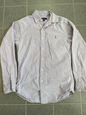 Ljuslila skjorta från Polo Ralph Lauren - Klassisk ljuslila skjorta från Polo Ralph Lauren med broderad logga på bröstet. Med storleken S.