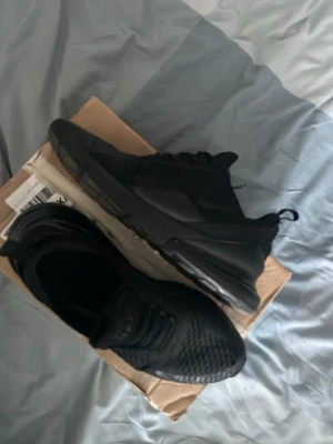 Helvita svarta sneakers Air Max stil - Säljer ett par helsvarta sneakers med sportig design och chunky sula. Skorna har meshdetaljer och dragflik bak där det står 'Air Max'. Perfekta för dig som gillar streetwear och vill ha en clean look till vardagsoutfiten. OBS VÄNSTRA SKOR LÅTER SOM LUFT NÄR MAN GÅR. SMÅ HÅL SOM INTE SYNS NÄR MAN HAR SVARTA STRUMPOR