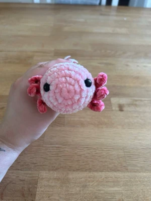 Virkad axelot - Supergullig handvirkad axelot i ljusrosa garn med mörkrosa detaljer och svarta säkerhetsögon. Perfekt som prydnad eller mysig liten maskot. Tillverkad i mjukt, fluffigt garn och får plats i handen.