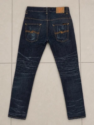 Nudie Jeans 31/32 - Snygga mörkblå jeans från Nudie Jeans med klassisk femficksdesign och orangea sömmar. Jeansen har en slim passform och slitningar på framsidan för en cool, använd look. Tillverkade i denim med stretch för extra komfort.