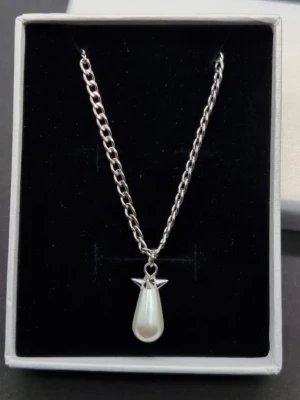 Handgjort halsband inspirerat av Maria Nilsdotter  - Snyggt halsband i silverfärgad metall med en droppformad vit pärla som hänge. Kedjan är medelgrov och ger ett modernt intryck. Perfekt accessoar för att lyfta din outfit med en elegant touch. Längd-40-45cm