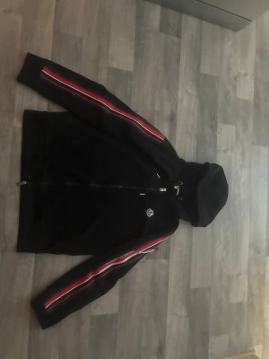 Svart Moncler hoodie  - Snygg svart tröja ifrån moncler. Säljer då ja sparar ihop pengar till att köpa bil. Minimalt använd och inga skador på tröjan. Storleken är L men är lite mindre i storleken så passar de flesta med storlek M också. 