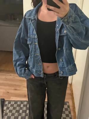 Oversized blå jeansjacka - Säljer en oversized blå jeansjacka med klassisk krage, knappstängning framtill och två bröstfickor med lock. Jackan har en avslappnad passform och är tillverkad i tåligt denimtyg. Perfekt att slänga över en t-shirt eller hoodie för en cool look.