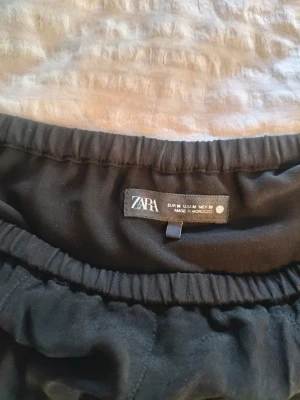 Zara kjol - Säljer en svart kjol med volang och asymmetrisk kant. Kjolen har en flowy look och resår i midjan för skön passform. Perfekt för dig som gillar en lite bohemisk och avslappnad stil.