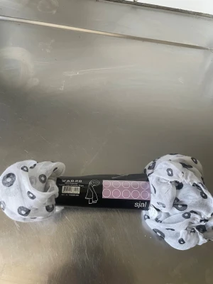 Vit sjal med svarta cirklar - Säljer en tunn och lätt vit sjal med svarta cirkelmönster. Sval och mjuk i 100% polyester, perfekt att slänga över axlarna för en cool och avslappnad look. Enkel att matcha med olika outfits och passar året runt.