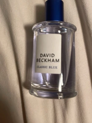David Beckham Classic Blue  -  Ny parfym och Fräsch parfym från David Beckham, Classic Blue. Flaskan är cylindrisk i genomskinligt glas med blått lock och ljusblå vätska. Enkel och stilren design med vit etikett och blå text. Perfekt för dig som gillar maskulina och sportiga dofter. 