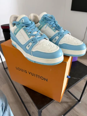 Louis Vuitton blåvita sneakers - Säljer ett par riktigt snygga Louis Vuitton sneakers i vitt och ljusblått läder. Kommer med box och extra snören mm. Använda 3 gånger!!!