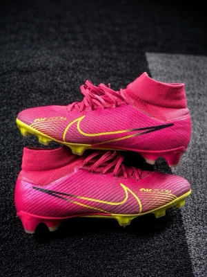 Nike rosa fotbollsskor med socka - Säljer ett par grymma rosa Nike fotbollsskor med hög socka och gula detaljer. Skorna har snörning, gult swoosh-märke och gult mönster på sulan. Ovandelen är i syntetmaterial för bra bollkontroll och passform. Perfekta för dig som vill sticka ut på planen!