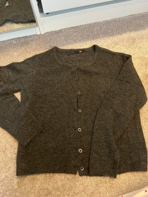 Stickad kofta - Mysig mörkgrå kofta från 157 med rund halsringning och knäppning framtill. Koftan har långa ärmar och ribbade muddar vid ärmslut och nederkant. Perfekt att slänga över en t-shirt eller linne för extra värme.