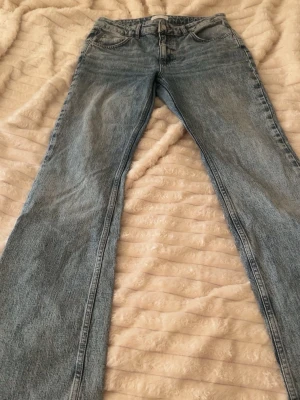 Blå raka jeans med hög midja - Säljer ett par klassiska blå jeans med rak passform och hög midja. Jeansen har fem fickor och stängs med dragkedja och knapp. Materialet är denim i 100% bomull och färgen är ljusblå tvätt. Perfekta till en avslappnad stil.