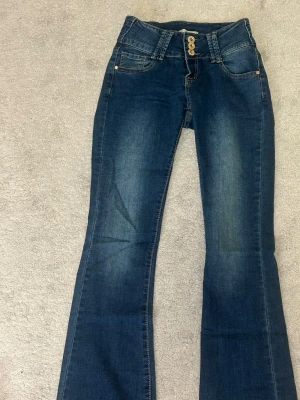 Mörkblå bootcut lågmidjade jeans  - Sååå Snygga mörkblå bootcut lågmidjade jeans med tre dekorativa guldknappar i midjan. HELT OANVÄNDA, hör av er vid intesss och frågor 🥰🤗🤩🤩🤩 passar nån som har XS /S 