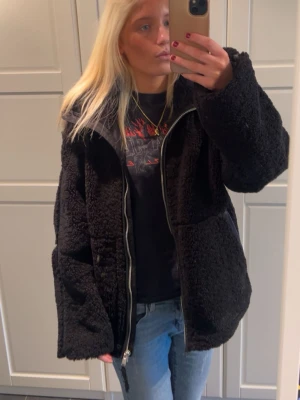 Svart oversized teddyjacka med dragkedja - Mysig svart teddyjacka i oversized modell med stor mysig krage och dragkedja framtill. Jackan har två sidofickor och är gjord i fluffigt, mjukt material. Superskön när det är kallt ute🖤