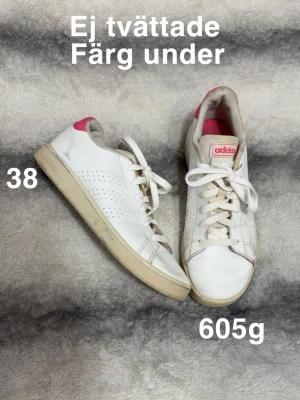 Vita Adidas sneakers med rosa detalj - Snygga vita sneakers från Adidas med klassisk låg profil och rosa detalj på hälen. Skorna har perforerade sidor, vita snören och beige sula. Perfekta för en avslappnad och sportig stil. 🌸 Ej tvättade. Har fått färg under. Storlek 38 