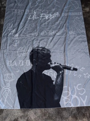 Svartgrå väggbodnad, Lil Peep motiv - Mjuk och stor filt i svart och grått med tryck av en sjungande person med mikrofon. Bakgrunden har olika texter och graffiti-liknande illustrationer. Perfekt att mysa med i soffan eller sängen.
