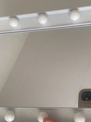 Rektangulär sminkspegel med LED-lampor - Snygg sminkspegel i rektangulär form med vit ram och inbyggda runda LED-lampor runt hela spegeln. Lamporna ger ett varmt, mjukt ljus som är perfekt för sminkning. Spegeln har en modern och stilren design som passar perfekt på sminkbordet.