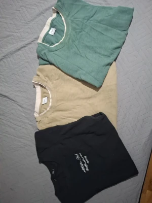Tre basic t-shirts i olika färger - Säljer tre stilrena t-shirts i grönt, beige och svart. Alla har rund halsringning och korta ärmar. Den svarta har ett diskret tryck på bröstet medan de andra är enfärgade. Perfekta till vardags och lätta att matcha med olika outfits.