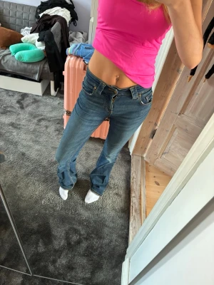 Blå bootcut jeans med låg midja - Säljer ett par blå bootcut jeans med låg midja och klassiska fickor både fram och bak. Jeansen har en snygg tvätt och sitter tajt över höfterna för en trendig look. Perfekta för dig som gillar en avslappnad men ändå stilsäker stil.