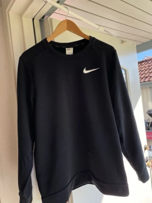 Svart sweatshirt från Nike - En stilren svart sweatshirt från Nike med klassisk vit Swoosh-logga på bröstet. Tröjan har rund halsringning och långa ärmar. Perfekt för en sportig och avslappnad look. Materialet känns mjukt och bekvämt mot huden. Tror storleken ska vara S men är större så skulle nog passa M bättre.