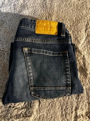 Blå raka jeans med slitningar - Säljer ett par klassiska blå jeans med raka ben och diskreta slitningar. Jeansen har fem fickor och normal midja. Materialet är denim i bomull och de har en avslappnad passform som passar till det mesta.