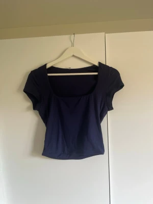 Mörkblå croppad topp med kort ärm - Snygg mörkblå croppad topp med fyrkantig ringning och korta ärmar. Tillverkad i mjukt bomullsliknande material och har en slim passform som framhäver figuren. Perfekt att matcha med höga jeans eller kjol.