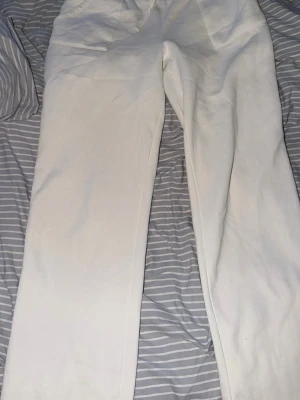 Vita raka mjukisbyxor med fickor - Säljer ett par vita mjukisbyxor med raka ben och band i midjan. Byxorna har två fickor framtill och är gjorda i ett mjukt och skönt material, perfekt för chill dagar. Passar dig som gillar en clean och enkel stil.