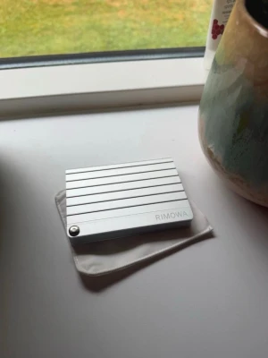 Silver plånbok i aluminium från Rimowa - Snygg och stilren plånbok från Rimowa i silverfärgad aluminium. Plånboken har ett modernt, räfflat mönster och kompakt design som gör den enkel att bära med sig. Perfekt för kort och sedlar, och levereras med en liten tygpåse.