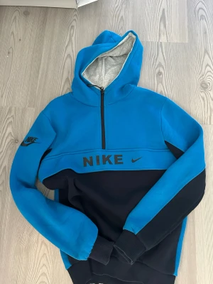 Blå och svart Nike hoodie med dragkedja - Snygg hoodie från Nike i blått och svart med halv dragkedja. Storlek S