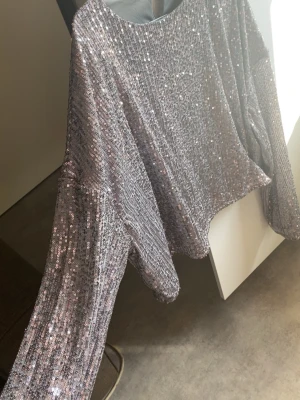 Glittrig tröja. - Säljer en glittrig tröja eller festtop som är lila med lite silver ton.de är Satintyg under och den e bekväm att ha på sig. Den har utsvängda armar.