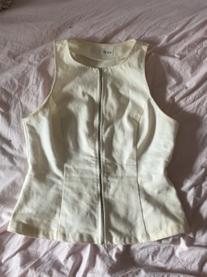 Vit ärmlös topp med dragkedja från Zara  - Snygg vit ärmlös topp med figurnära passform och dragkedja framtill. Tillverkad i ett kraftigare bomullstyg som ger en stilren och modern look. Perfekt att matcha med jeans eller kjol för en trendig outfit.
