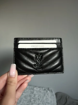 Korthållare svart - Snygg svart korthållare i quiltat läder med klassisk logga framtill. Fodralet har flera fack för kort och en stilren, minimalistisk design som passar perfekt i fickan. Perfekt accessoar för dig som gillar lyxiga detaljer. Ny och aldrig använd 