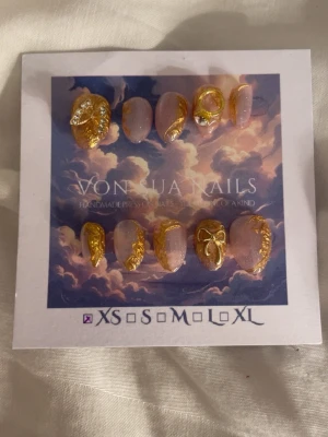 Press-on naglar med gulddekor - Handgjorda press-on naglar i en mjuk rosa nyans med skimrande finish. Naglarna har detaljer i guld, inklusive 3D-mönster, stenar och en liten rosett. Ovala till mandelformade och riktigt lyxiga – perfekta för dig som vill sticka ut.